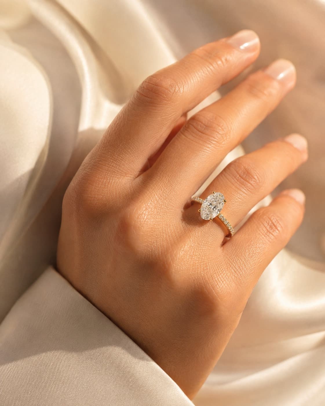 Oval diamond engagement ring worn on hand over silk